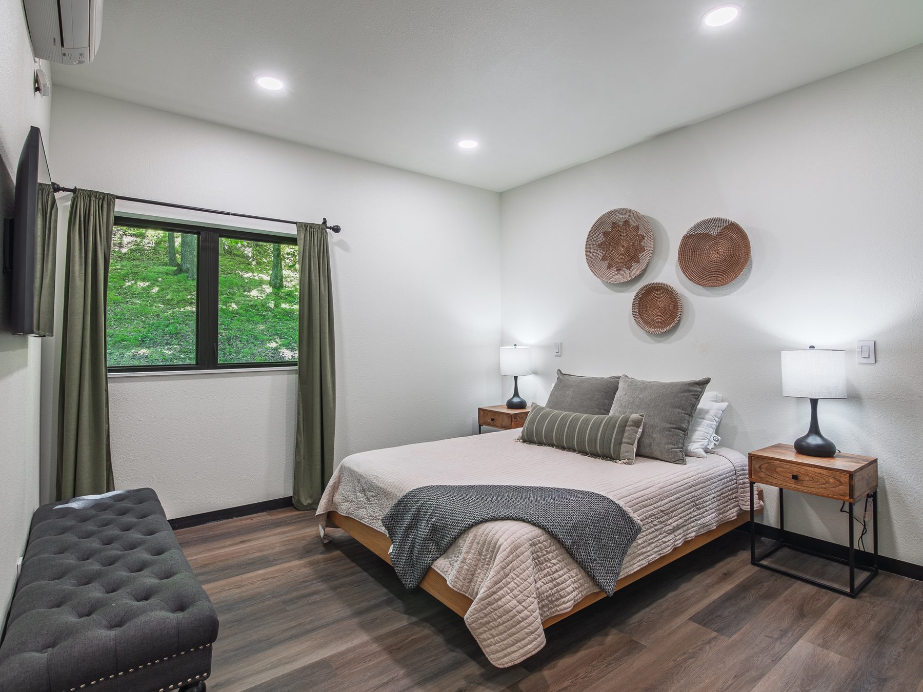 Arrow Lane bedroom with woven wall baskets, olive curtains and a window onto the wooded hillside