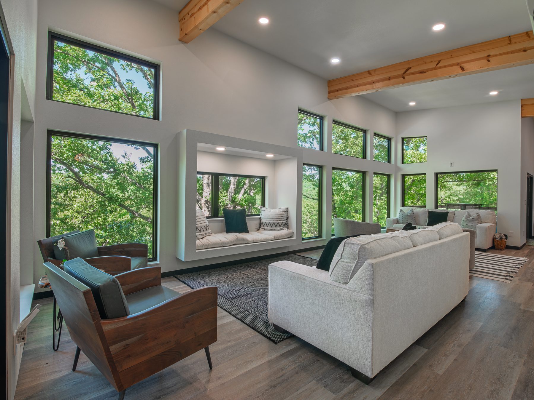 Vaulted Arrow Lane living room with exposed cedar beams, a wall of windows into the tree canopy and a built-in window seat