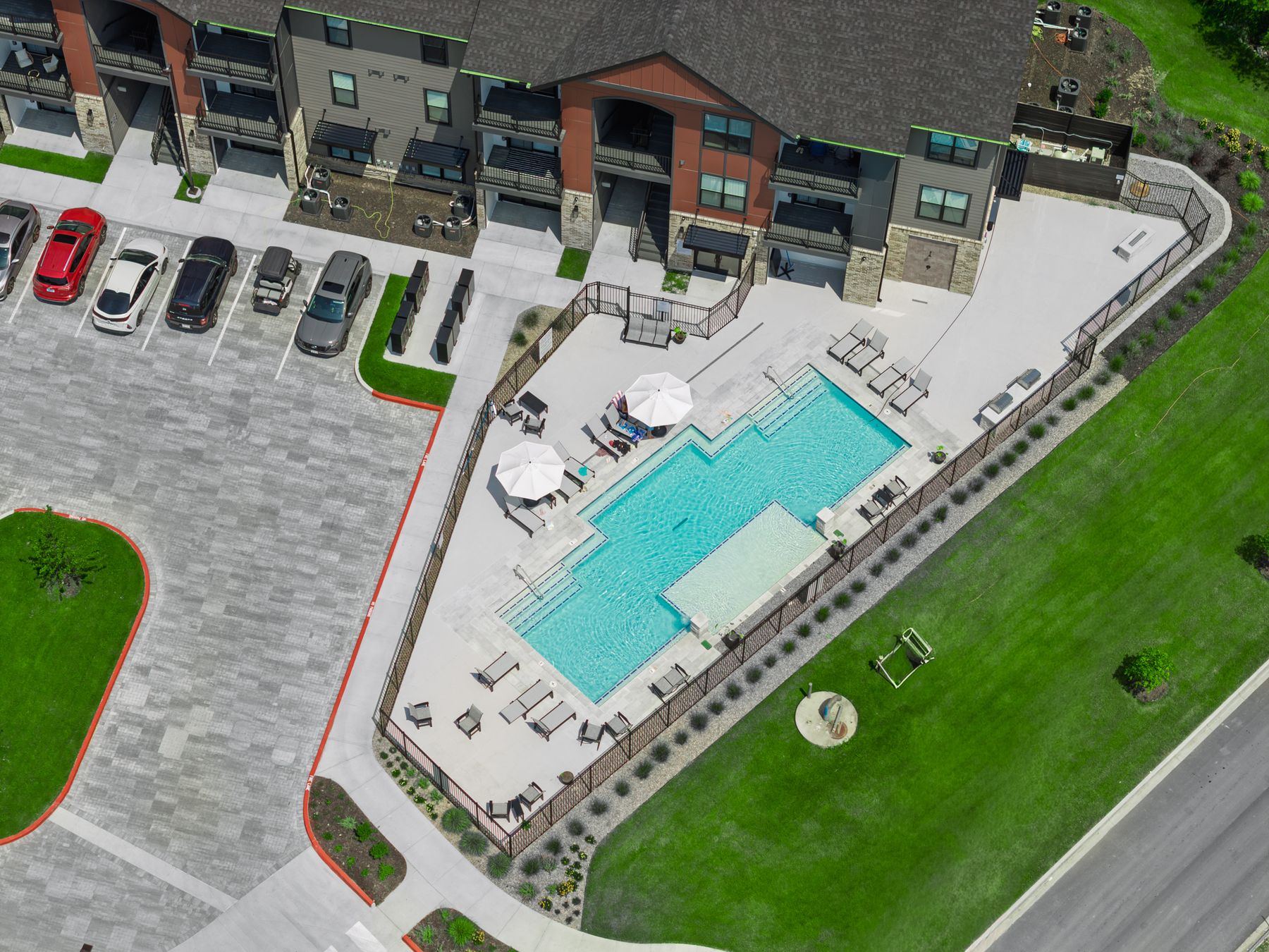 Top-down aerial of the complex's fenced pool deck, with umbrellas and loungers between the buildings and the lawn